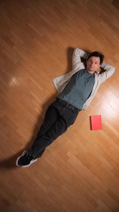 A person following a simple movement guide shown on a tablet, seated on a wooden floor in natural morning light